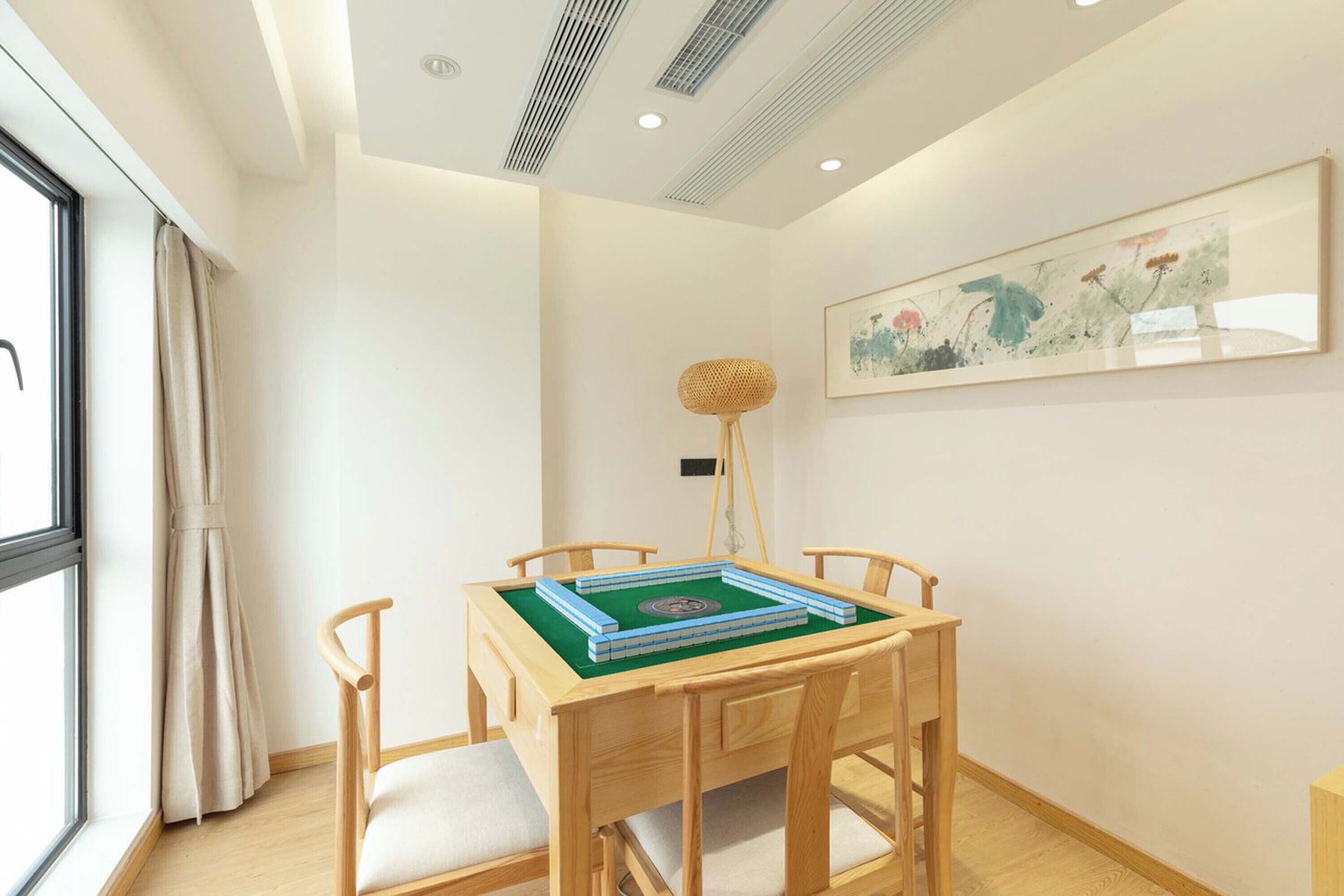 Una habitación con una mesa de comedor preparada para cuatro, una ventana con cortinas, una lámpara de pie y una obra de arte enmarcada en la pared.