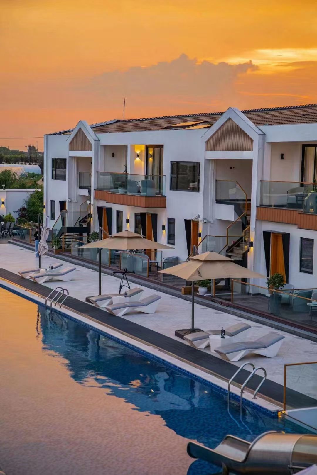 Un hotel moderno con piscina, area relax esterna e vista sul tramonto.