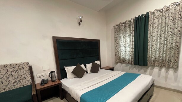 A hotel room with a bed, a nightstand, a power outlet, a telephone, and a window with curtains. - The Mohan By LIVIQ Delhi Railway Station (New Delhi)