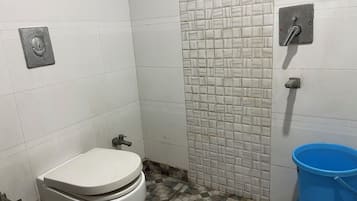 A small bathroom with a toilet, a blue bucket, and a tiled wall.