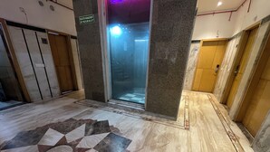 An interior corridor with a marble floor, a glass elevator door, and a sign indicating a helpline number. - The Mohan By LIVIQ Delhi Railway Station (New Delhi)