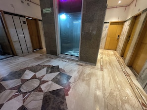 Corredor interior com piso de mármore, porta de elevador de vidro e um aviso com número de telefone de ajuda.