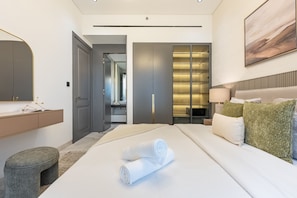 Ett modernt hotellrum med en stor säng, ett sängbord, en spegel, en garderob och ett badrum som syns genom en öppen dörr.