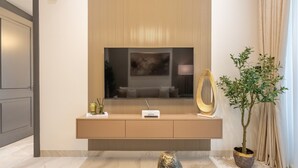 A modern living room with a large flat-screen TV mounted on a wall, a console table with decorative items, a potted plant, and a unique sculpture. - Just a Stone Throw from the Public Park and a Short Drive from Butterfly Garden (Dubai)