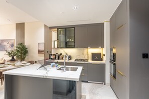 A modern kitchen with a central island, built-in appliances, and a dining area with a table set for two. - Just a Stone Throw from the Public Park and a Short Drive from Butterfly Garden (Dubai)