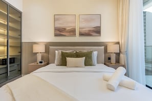 Ein Hotelzimmer mit einem Bett, zwei Nachttischlampen, einem Nachttisch, einem großen Fenster mit Vorhängen und zwei gerahmten Bildern an der Wand.