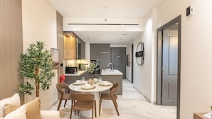 A modern kitchen with a central island, a dining area with a round table and chairs, and a hallway leading to a door. - Just a Stone Throw from the Public Park and a Short Drive from Butterfly Garden (Dubai)