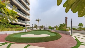 A landscaped outdoor area with a central green lawn, surrounding pathways, and a palm tree. - Just a Stone Throw from the Public Park and a Short Drive from Butterfly Garden (Dubai)