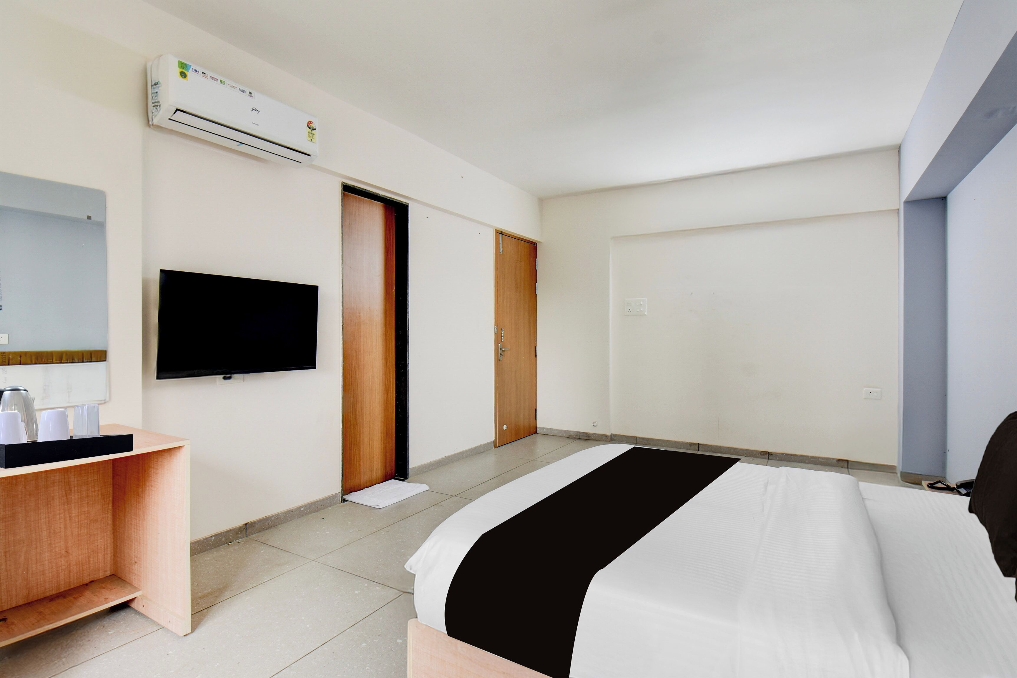 Habitación de hotel con cama, escritorio con espejo, televisor de pantalla plana, puerta de madera y unidad de aire acondicionado.