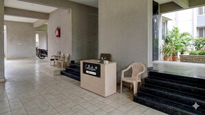 Un'area di accoglienza con reception, sedute, estintore e una scala che conduce a una zona esterna con piante in vaso.