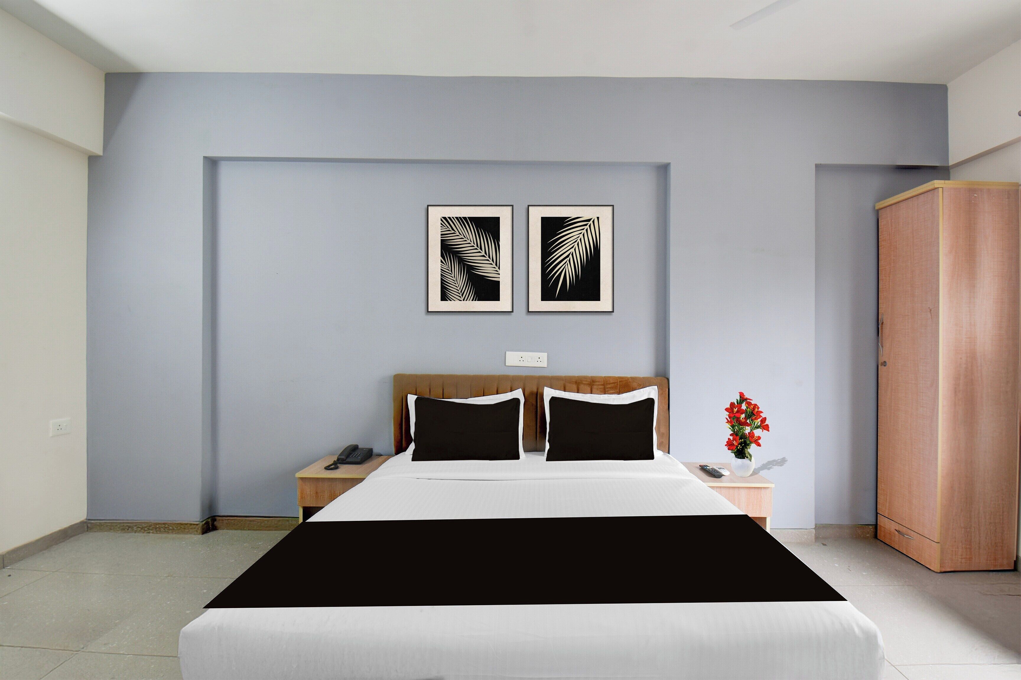 A hotel room with a bed, two nightstands, a wardrobe, and two framed leaf art pieces on the wall.