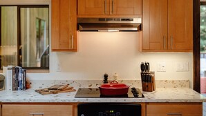 Une cuisine avec des armoires en bois, une hotte de cuisinière en acier inoxydable, une casserole rouge sur la plaque de cuisson et un bloc à couteaux posé sur le plan de travail.