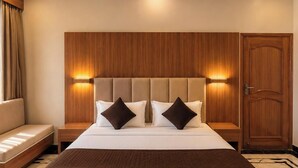 Habitación de hotel con una cama grande, cabecera de madera, lámparas de noche, un armario de madera y un sofá.