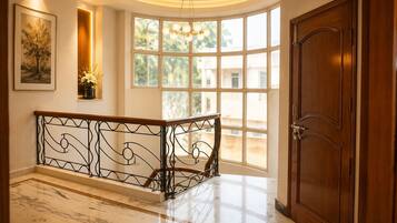 Un pasillo con piso de mármol, una puerta de madera y una barandilla curva con un aplique de luz.
