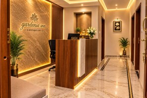 A reception desk with a sign reading 'gardenia inn,' a reception area, and a hallway with a potted plant. - HOTEL GARDENIA INN (Gwalior)