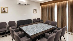 Un salón de conferencias con una gran mesa, sillas, una araña y cortinas, además de cuadros en las paredes.