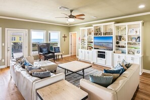 A living room with a sofa, armchairs, a coffee table, and a television. There is a balcony with a view of the ocean. - Beachy Keen- 2nd Row w/ great Views, Pool Table! 3 Bedroom, 3 Bath- Sleeps 10 (Crystal Beach)
