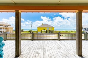 A wooden deck with a view of a beach and a yellow building. - Beachy Keen- 2nd Row w/ great Views, Pool Table! 3 Bedroom, 3 Bath- Sleeps 10 (Crystal Beach)