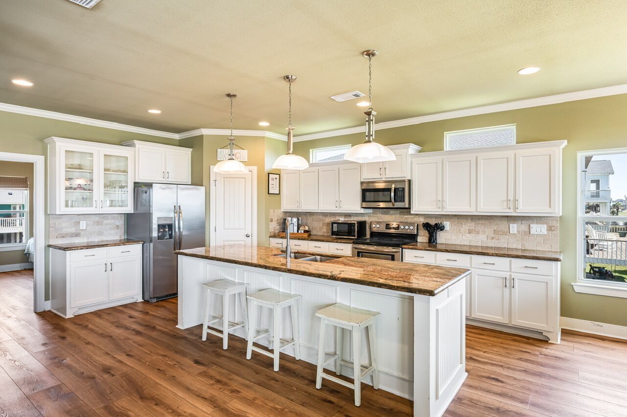 A modern kitchen with white cabinetry, a central island with stools, stainless steel appliances, and pendant lighting.