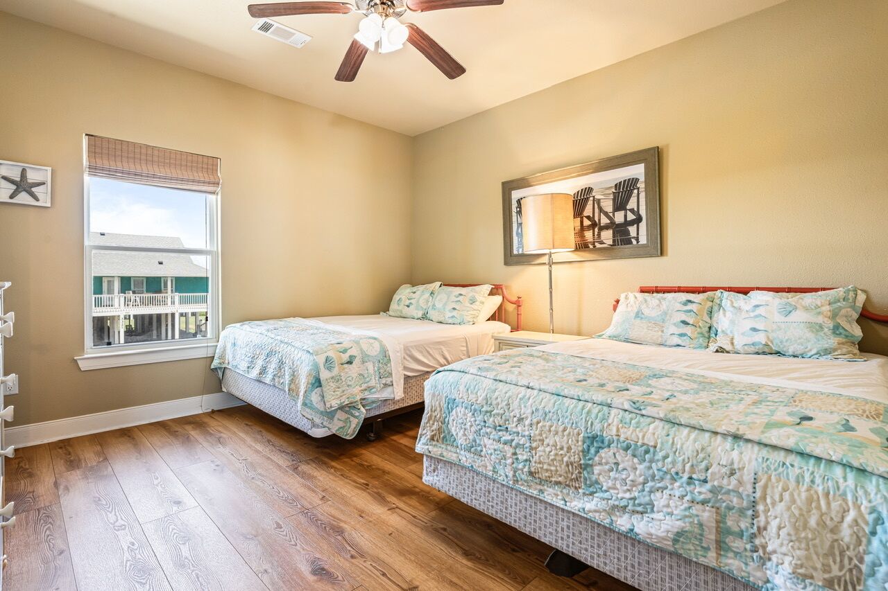 A bedroom with two beds, a ceiling fan, a window with blinds, and a framed picture on the wall.