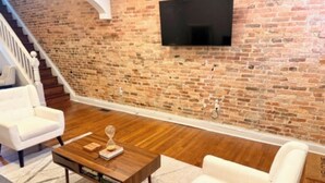 Ein Wohnzimmer mit Backsteinwand, Flachbildfernseher, Holztisch und weißem Sofa sowie einer Treppe.