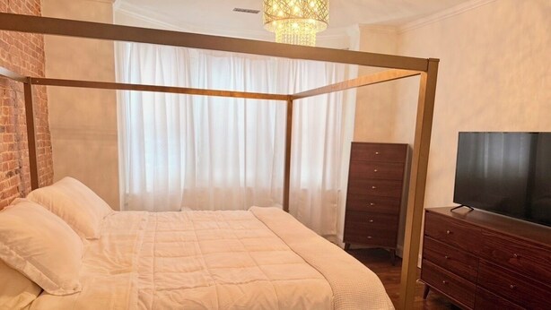 Ein Bett mit Himmel, ein Holzgestell, ein Fernseher auf einer Holzkommode und eine Chandelier.