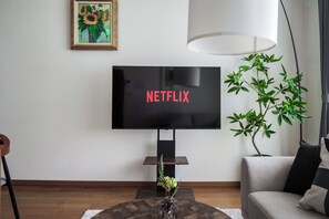 A living room with a flat-screen TV displaying 'NETFLIX' in red letters, a large potted plant, a sofa, and a coffee table with a vase of flowers. - HARMONY OTARU (Otaru)