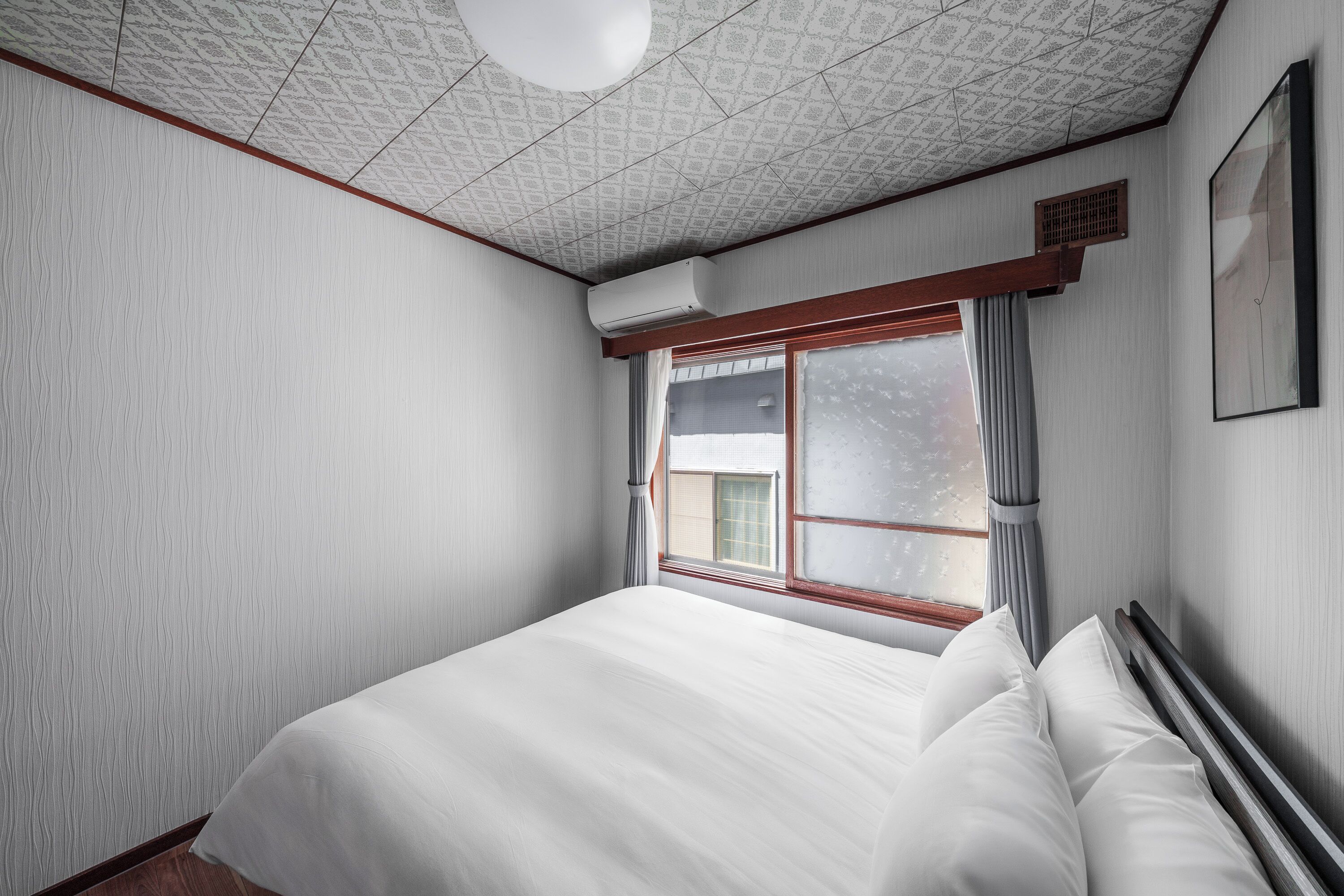 A bedroom with a large bed, a window with curtains, a ceiling fan, and a wall-mounted air conditioner.