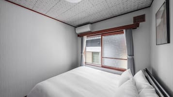 A bedroom with a large bed, a window with curtains, a ceiling fan, and a wall-mounted air conditioner.