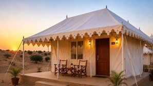 A desert tent with a wooden door, two windows, and a set of chairs on a platform.