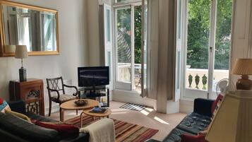 A living room with a television, a sofa, a coffee table, and a large window with an open door.