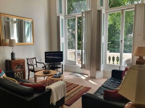 Ett vardagsrum med en tv, en soffa, ett soffbord och ett stort fönster med en öppen dörr.