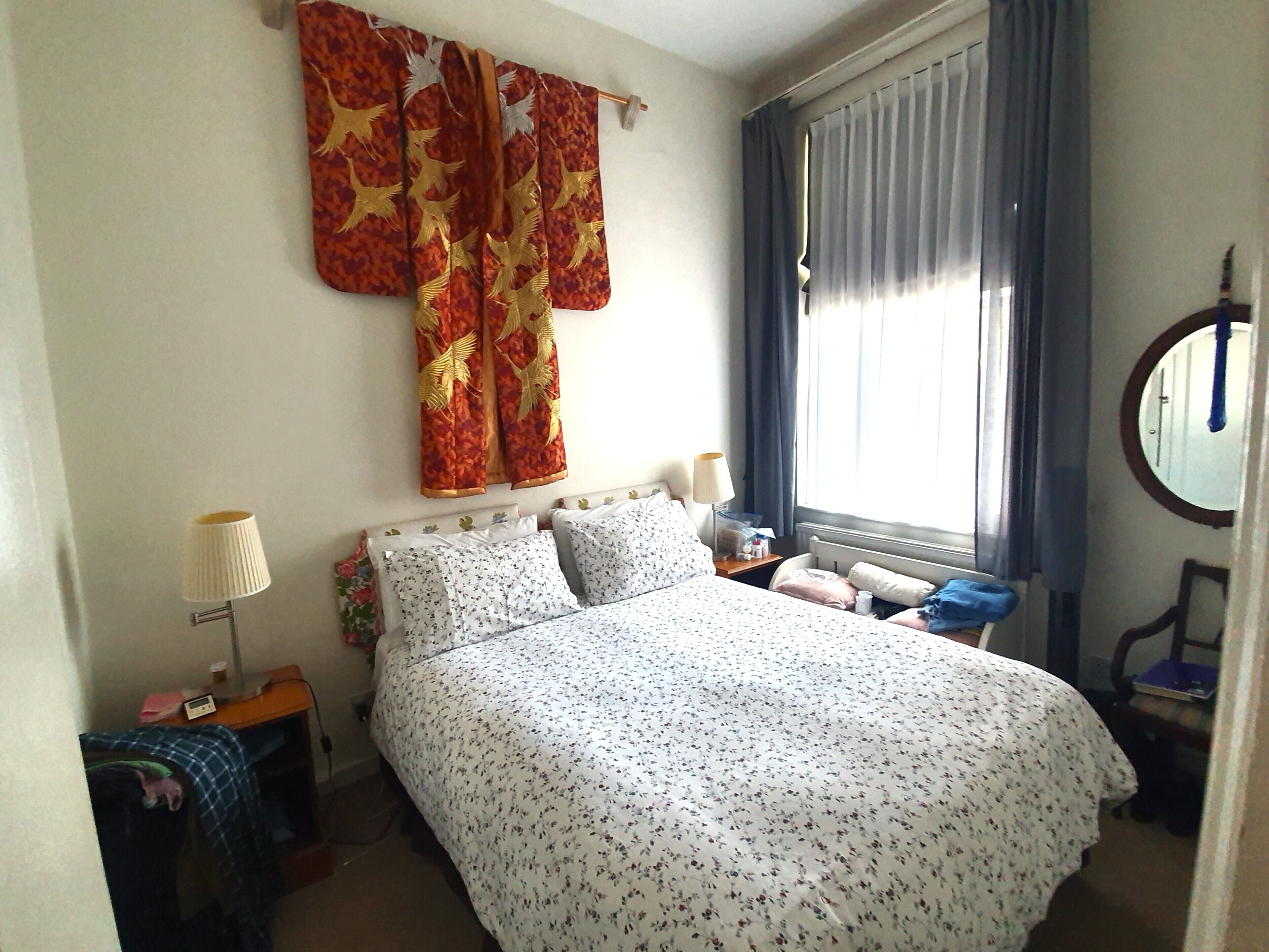 A bedroom with a bed, a nightstand, a lamp, a window with curtains, and a mirror.