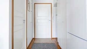 Un pasillo estrecho con puertas blancas, suelo de madera y un pequeño tapete en la entrada.