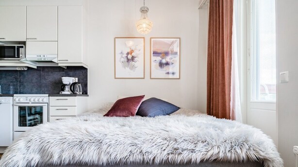 Un dormitorio moderno con una cama grande, una kitchenette con microondas y cafetera, y dos obras de arte enmarcadas en la pared.