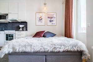 Um quarto moderno com uma cama grande, uma kitchenette com micro-ondas e máquina de café, e duas obras de arte emolduradas na parede.