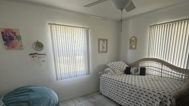 Un dormitorio con cama, ventilador de techo, sillón de plumas y alfombra.