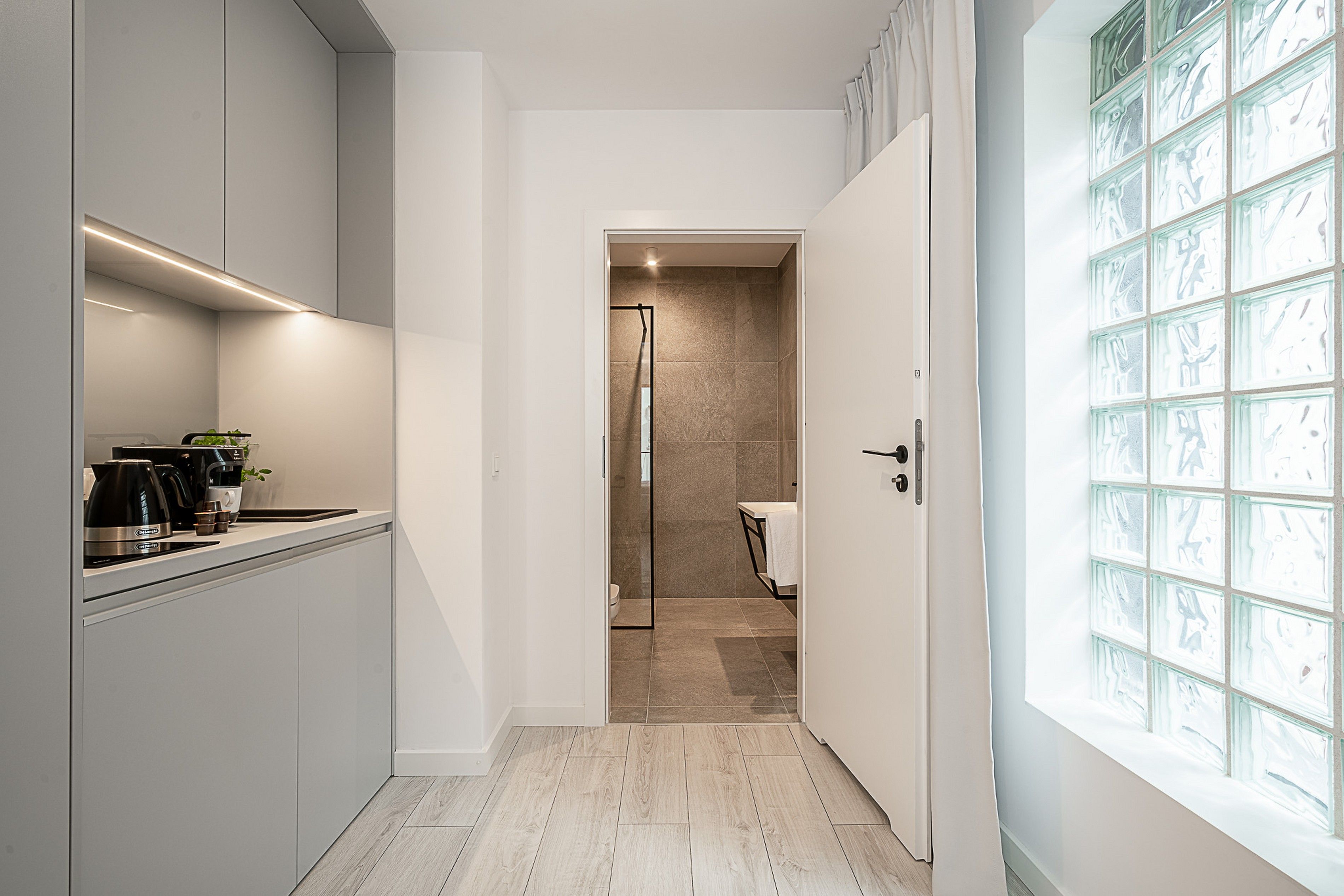 Une cuisine moderne équipée d’une machine à café, d’une plante et d’une porte en verre donnant sur une salle de bain avec douche et toilettes.