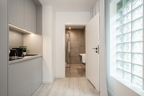 Una cocina moderna con cafetera, una planta y una puerta de cristal que da a un baño con ducha e inodoro.