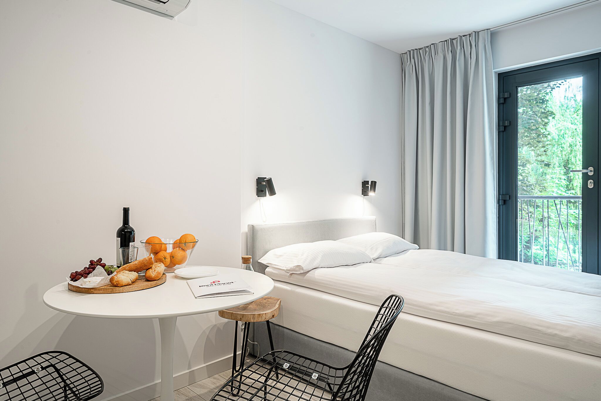 Ein Hotelzimmer mit Bett, einem kleinen Tisch mit Speisen, einer Flasche und einem Sessel.
