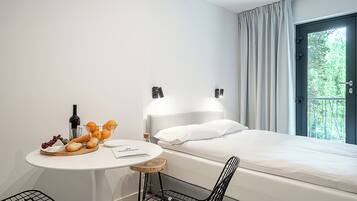 Ein Hotelzimmer mit Bett, einem kleinen Tisch mit Speisen, einer Flasche und einem Sessel.