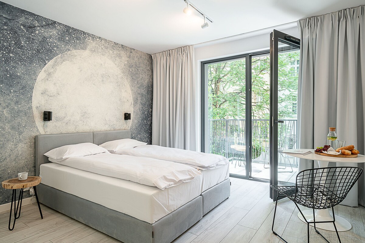Un dormitorio moderno con una cama grande, una mesita con artículos de desayuno y un balcón con vistas a zonas verdes.