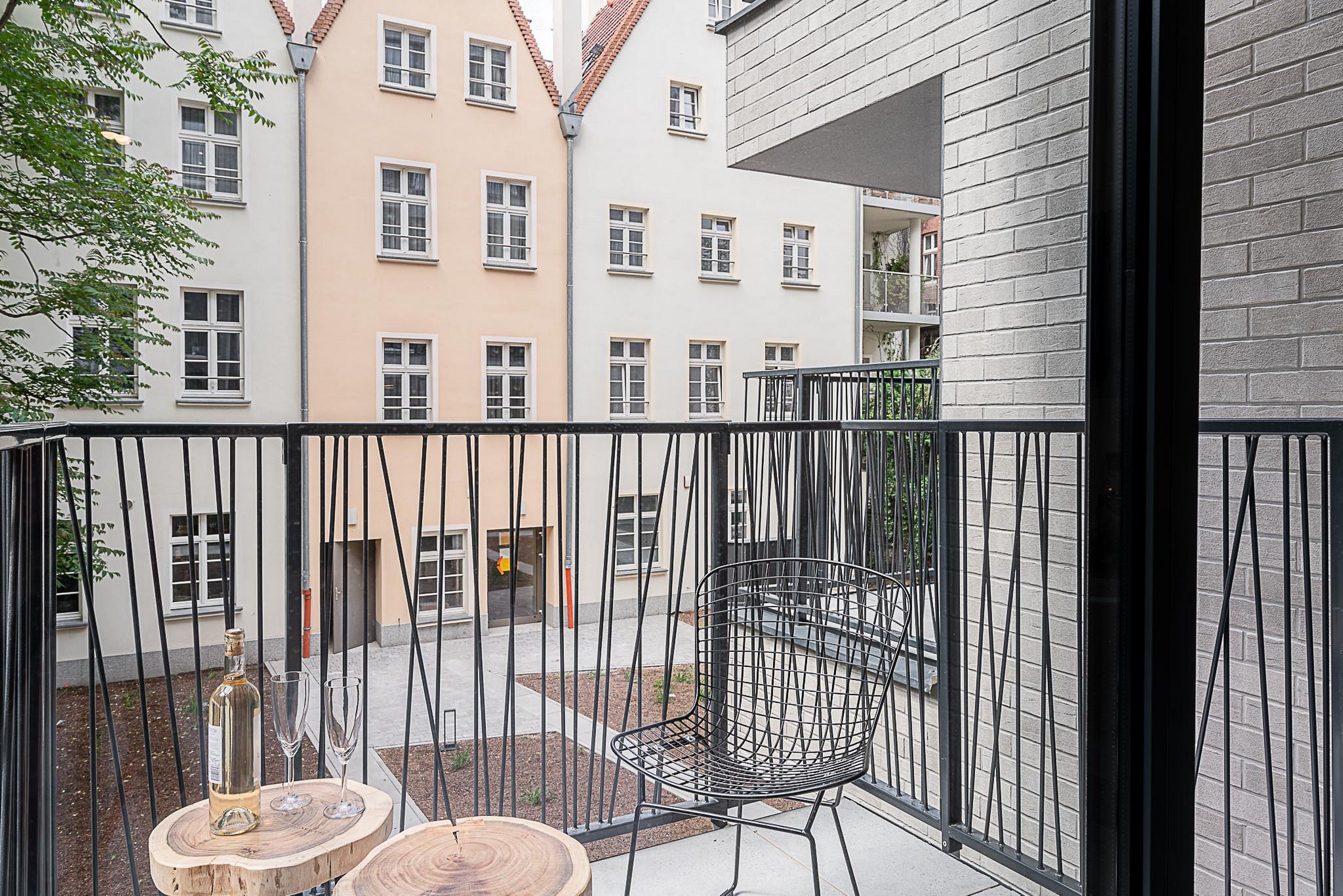 Ein Balkon mit einem Metallstuhl und einem kleinen Tisch, auf dem eine Flasche und Gläser stehen.