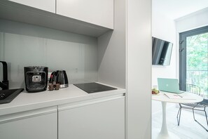 Una cocina moderna con una cafetera, un hervidor y una computadora portátil sobre una mesita.