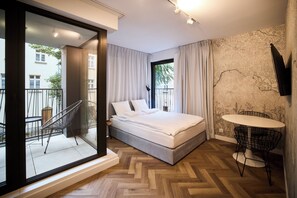 Un dormitorio moderno con cama, un balcón con una silla, una mesita y un televisor montado en la pared.
