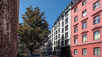 Straßenansicht mit mehrstöckigen Gebäuden, einem Baum und parkenden Autos.