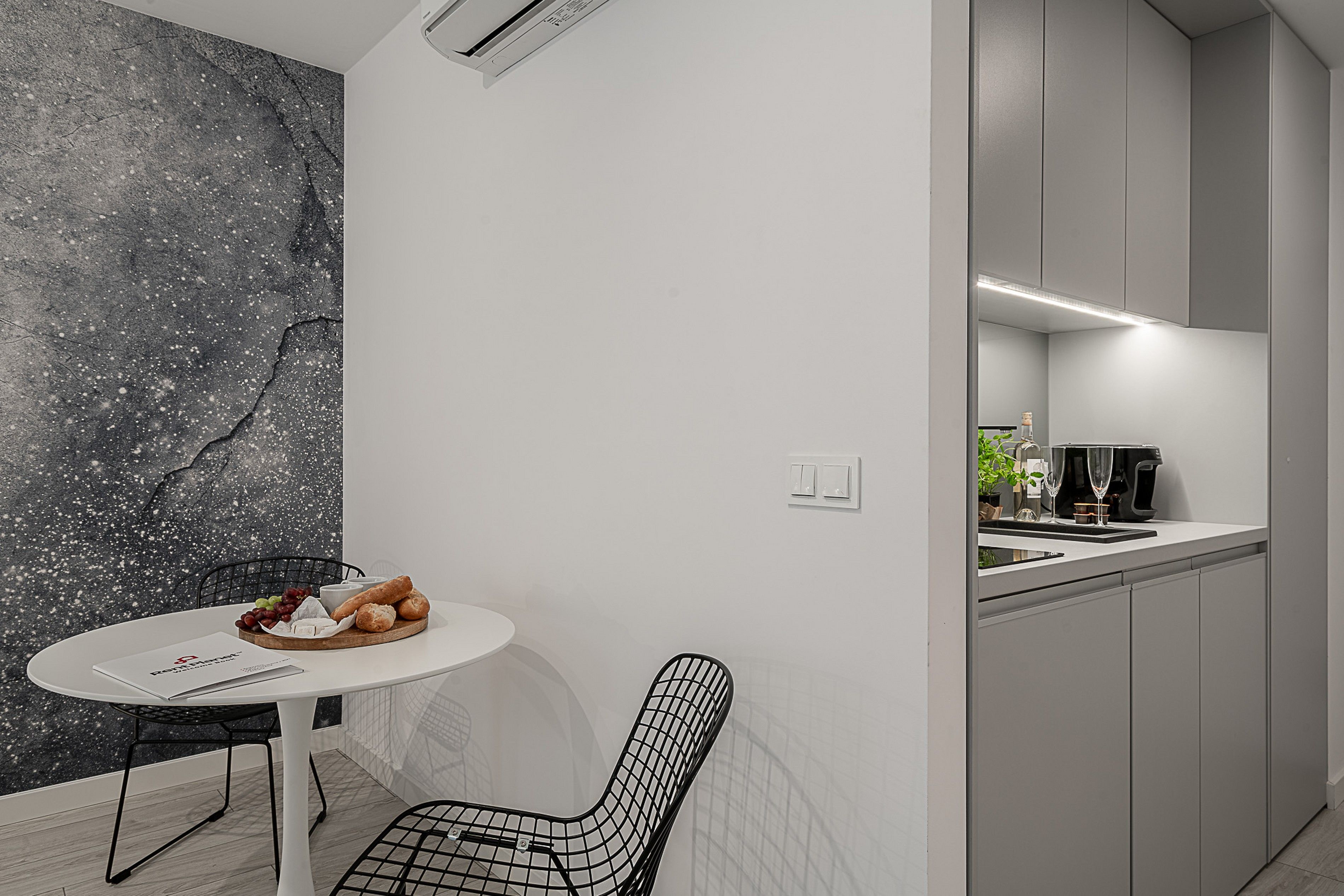 Una cocina moderna con salpicadero de mármol, un comedor con mesa redonda y sillas, y una cafetera.