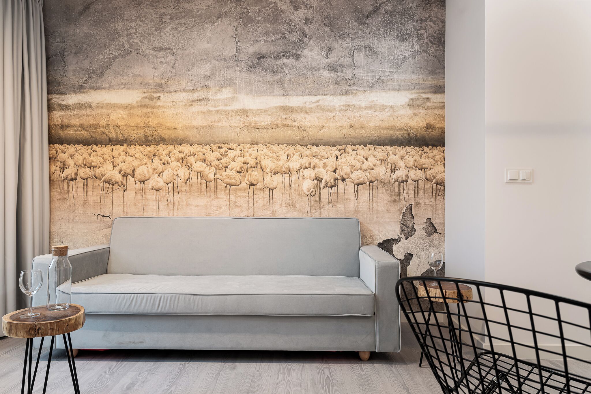 Ein Wohnzimmer mit grauem Sofa, einem Holztisch und einer Wandmalerei von Flamingos.