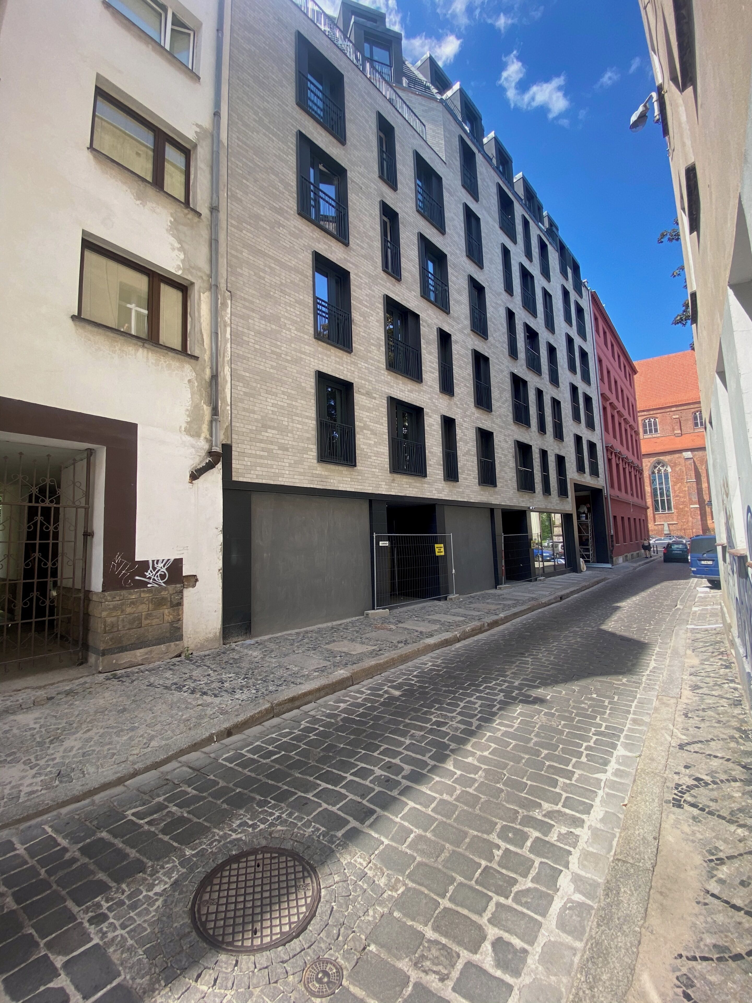 A cobblestone street with a modern building featuring multiple windows and balconies.