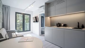 A modern kitchen with a built-in oven, a coffee machine, and a sink. There is a dining area with a table and chairs, and a window with curtains.